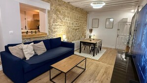 A living room with a blue sofa, wooden coffee table, stone wall, and a TV. - STUNNING DUPLEX IN THE HEART OF THE CITY CENTER WITH UNDERGROUND PARKING INCLUDED, 10 MINUTES FROM PARIS (Rueil-Malmaison)