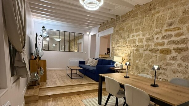 A modern living space with a stone wall, a blue sofa, a wooden dining table, and a kitchen area. - STUNNING DUPLEX IN THE HEART OF THE CITY CENTER WITH UNDERGROUND PARKING INCLUDED, 10 MINUTES FROM PARIS (Rueil-Malmaison)