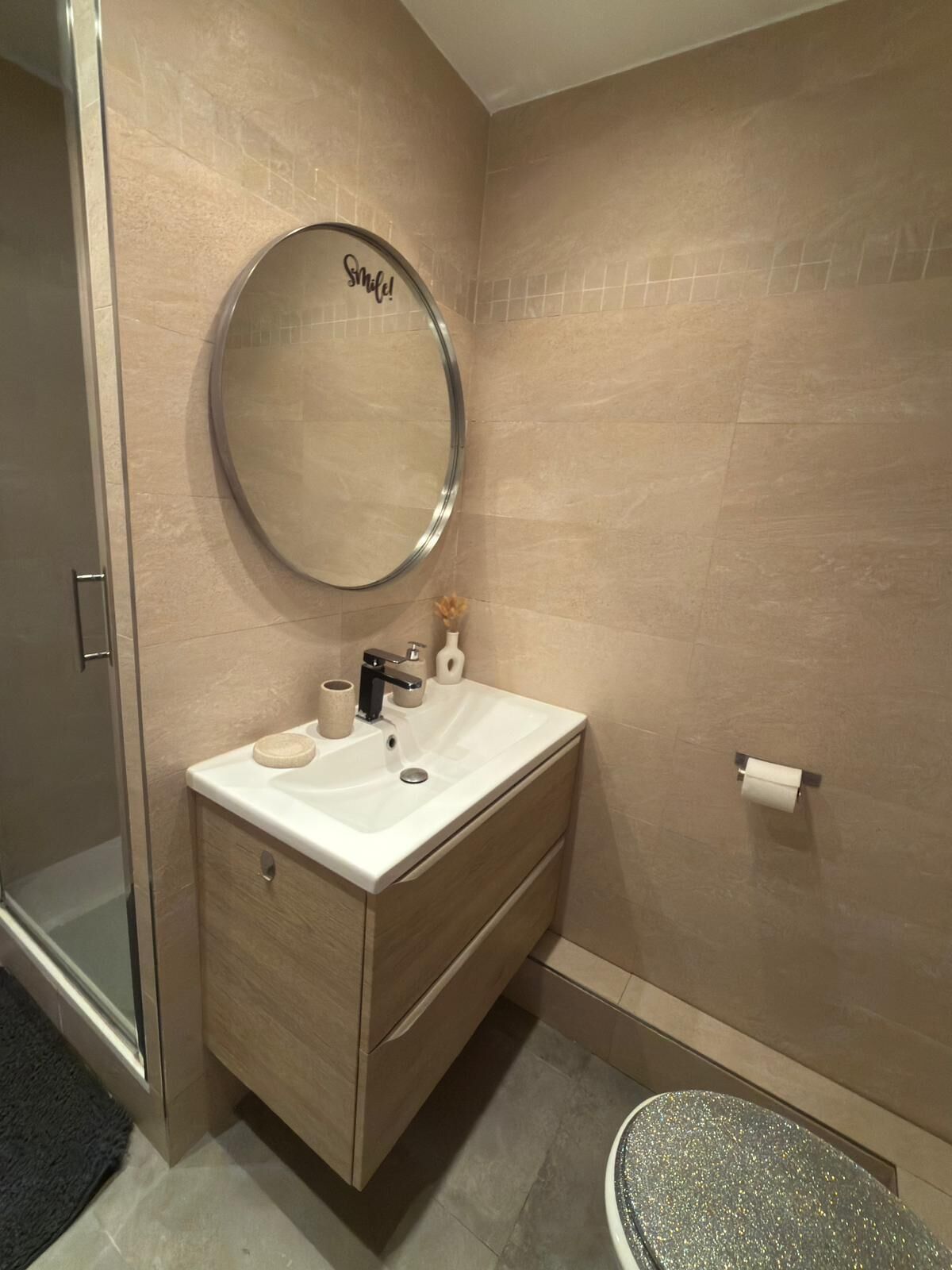 A bathroom with a round mirror, a sink, a toilet, and a shower area.