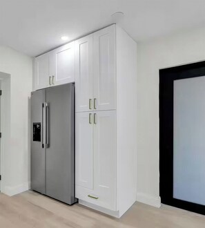 Eine moderne Küche mit weißen Schränken, einem Edelstahlkühlschrank und einer schwarzen Tür.