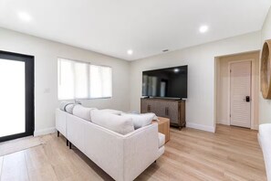Ein Wohnzimmer mit Sofa, Fernseher, Holzschrank und einer Tür.