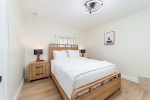 Ein Schlafzimmer mit einem hölzernen Bett, Nachttischen mit Lampen, einem Deckenventilator, einem Wandbild und einem kleinen Korb.