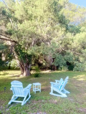 Eine Rasenfläche mit zwei Adirondack-Stühlen und einem kleinen Tisch.