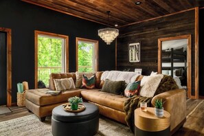 Ein gemütliches Wohnzimmer mit einem ledernen Ecksofa, einem runden Hocker, einem Couchtisch aus Holz und einer Deckenleuchte.