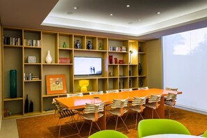 Un soggiorno moderno con una grande libreria in legno, un televisore a schermo piatto, un lungo tavolo da pranzo arancione con sedie e un'ampia finestra.