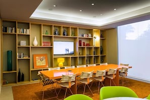 A modern living room with a large wooden bookshelf, a flat-screen TV, a long dining table with chairs, and a large window.