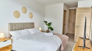 Un dormitorio ordenado con cama, mesita de noche, lámpara, decoración en la pared, planta en maceta y armario.