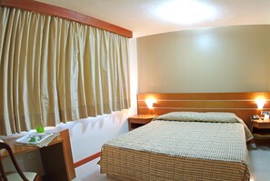 Une chambre d’hôtel comprenant un lit, des tables de chevet, un bureau avec une chaise et des rideaux.