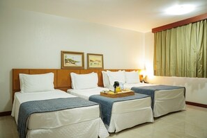Une chambre d’hôtel avec deux lits, une table de chevet avec une lampe, une fenêtre avec des rideaux et deux tableaux encadrés au mur.