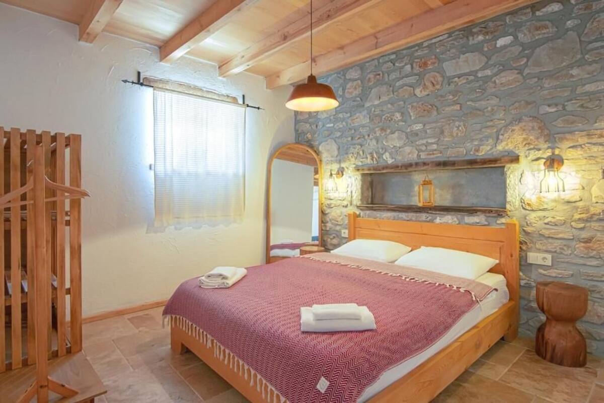 A bedroom with a stone wall, wooden bed, and a hanging light fixture.