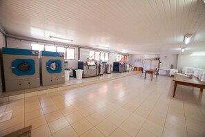A laundry facility with industrial washing machines, a table with folded clothes, and a tiled floor. - 2 Rooms | Cascavel Brazil Escape w/ Gym | 3.7 mi to Kart Racing Adventure (Cascavel)