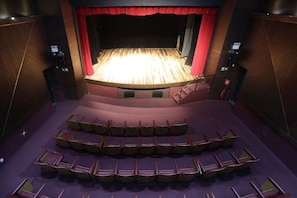 A theater with a stage, tiered seating, and red curtains.