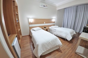 A hotel room with two beds, a wooden wardrobe, a desk, and a small table.