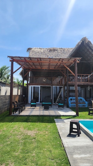 A wooden structure with a thatched roof, outdoor seating, and a swimming pool.