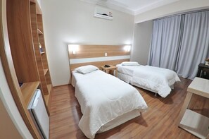 A hotel room with two beds, a wooden wardrobe, a desk, and a small table.
