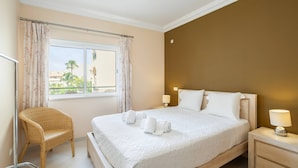 Ein Hotelzimmer mit Bett, Sessel, Nachttisch und einem fenster mit Vorhängen.