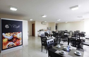 A dining area with tables and chairs, a kitchen in the background, and a large poster on the wall. - Central Exec Room | Free Breakfast | Steps to Local Dining & Xingu River Tours (Altamira)