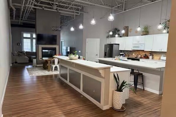 A modern kitchen with white cabinetry, a central island, pendant lighting, and a visible TV.