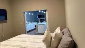 Una camera da letto con un letto, cuscini, una televisione e vista su cucina e sala da pranzo.