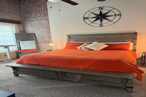 A bedroom with a large bed, a brick wall, a ceiling fan, and a compass wall decoration.