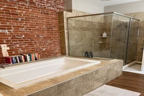 A modern bathroom with a large bathtub, a glass shower enclosure, and a brick wall.