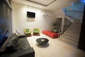 En moderne stue med sofa, to stole, en rød skammel, fjernsyn og trappe.