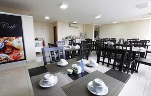 Spiseområde med borde dækket til servering, et køkken i baggrunden og et caféskilt på væggen.
