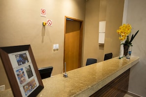 En receptionsdisk med et indrammet billede, et skilt med rygning forbudt, en brandalarm og en dør.