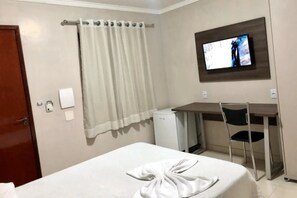Una habitación de hotel con cama, escritorio, televisor y cortina de ducha.