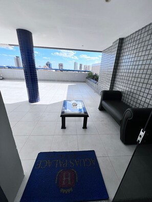 Una terrazza sul tetto con un tavolo in vetro, un divano nero e un tappetino blu con un logo.