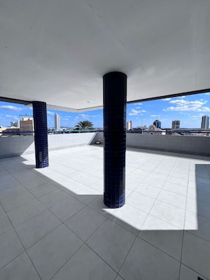 Eine großzügige Dachterrasse mit Fliesenboden und zwei markanten, blauen Säulen, die einen Blick auf die Stadt bietet.
