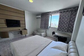 Ein Hotelzimmer mit Bett, Fernseher an einer Holzvertäfelung, einer Couch, einem kleinen runden Tisch und einem Fenster mit Vorhängen.