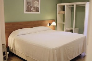 Ein ordentlich bezogenes Bett mit einem Holz-Kopfteil, einer Nachttischlampe und einem weißen Kleiderschrank mit Regalen.