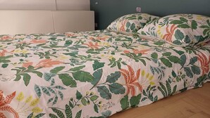 Sängyssä on kukallinen päiväpeite, pääty ja puulattia.