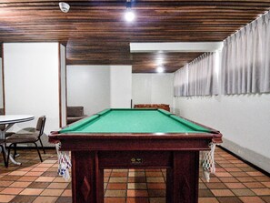 Ein Billardtisch in einem Raum mit Fliesenboden, einer Holzbalkendecke und einer weißen Wand mit Vorhang.