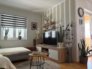 A modern living room with a flat-screen TV, a sofa, a coffee table, and potted plants. - Apartman Posedarje by Aneo Travel (Posedarje)