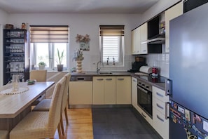 A modern kitchen with a wooden dining table, a built-in oven, and a refrigerator with magnets. - Apartman Posedarje by Aneo Travel (Posedarje)