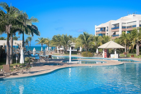 A resort pool area with palm trees, lounge chairs, and a gazebo. - Wai Wai #a204 Comfort Beachfront By Carpediem (Caucaia)