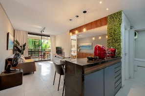 A modern kitchen with a central island, a dining area with a sofa, and a living room with a fan. - Wai Wai #a204 Comfort Beachfront By Carpediem (Caucaia)
