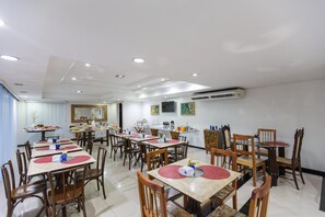 Uma sala de jantar com várias mesas e cadeiras, um aparelho de ar condicionado na parede e um espelho sobre o balcão.