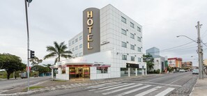Um hotel moderno com uma placa chamativa que diz 'HOTEL', um restaurante no térreo e uma área de estacionamento.