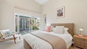 A bedroom with a bed, a chair, a bedside table, a lamp, and a picture on the wall. - Away Away - Surf Side Inverloch (Inverloch)