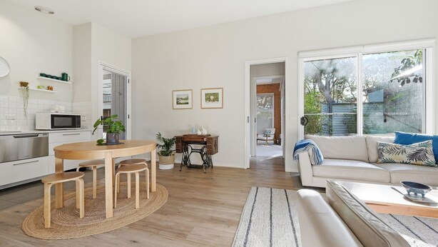 Eine moderne Küche mit Essbereich, einer Nähmaschine und einem Wohnzimmer mit Sofa und Blick ins Freie.