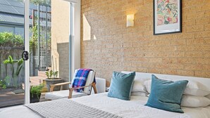 Ein Schlafzimmer mit Backsteinwand, einem Bett mit weißer Bettwäsche und Blick auf einen Garten durch eine Glastür.