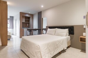 Ein modernes Hotelzimmer mit einem großen Bett, einem kleinen Schreibtisch und einer Küchenzeile.