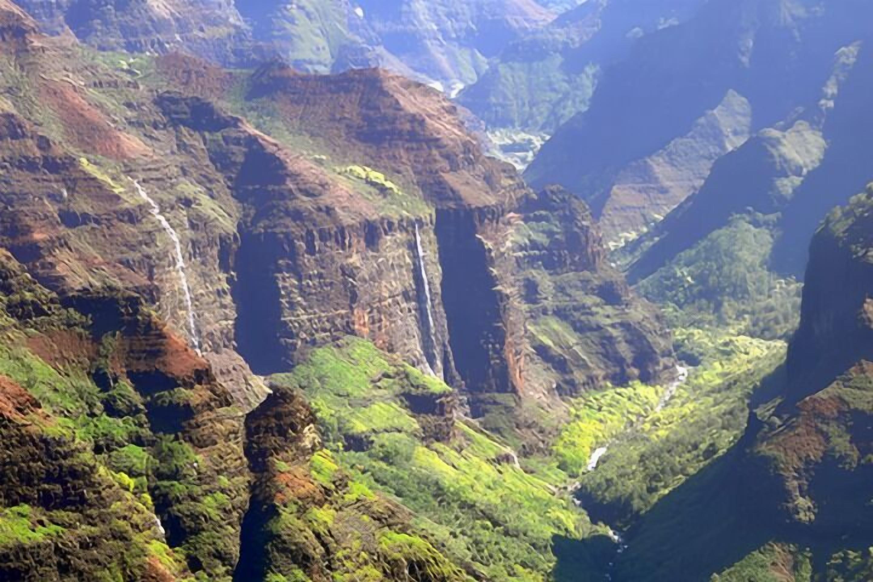 Een bergachtig landschap met een waterval en weelderige begroeiing.