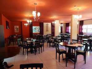 Un ristorante con diversi tavoli e sedie, lampadari sospesi e un'ampia finestra con tende.