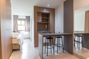 Habitació moderna amb cuineta, un llit i una finestra amb cortines.