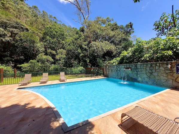 Piscina con muro in pietra, sedie a sdraio e cascata.