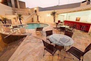 Un espace piscine agrémenté d’une table en verre et de chaises en osier, d’un escalier et d’un coin bar.
